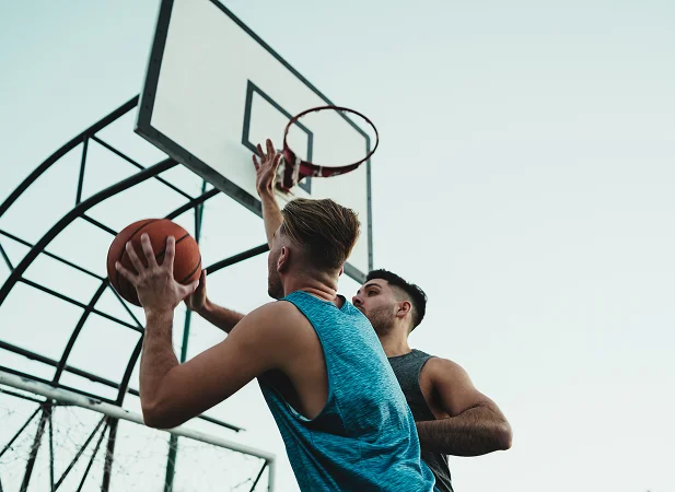 Two basketball players compete for a scoring opportunity beneath an outdoor basketball hoop during a dynamic match.