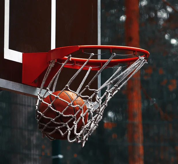 A basketball passes through the net, capturing a successful shot on an outdoor basketball court.