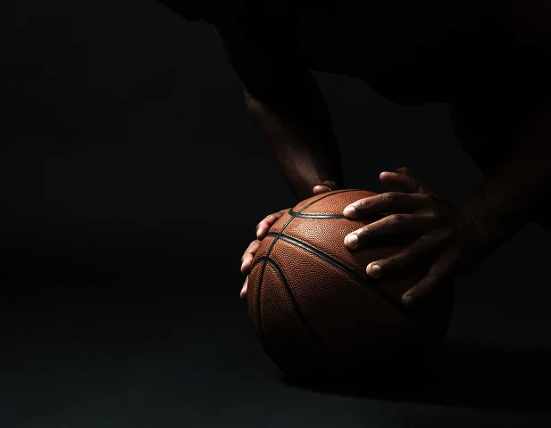 Close-up view of a player preparing for action while holding a basketball in a low-light sports setting.