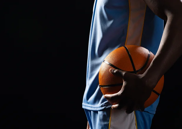 Basketball athlete holding a ball while wearing a sports uniform against a dark studio background.