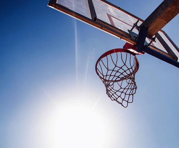 Outdoor basketball hoop and backboard photographed from below with a bright blue sky in the background.
